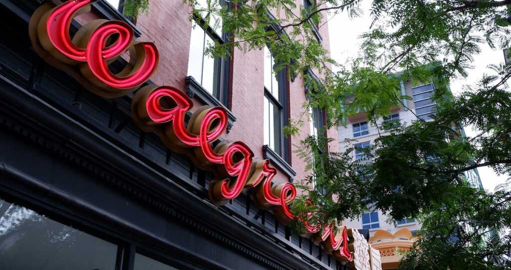 a neon walgreens sign shines through the trees on a brick building