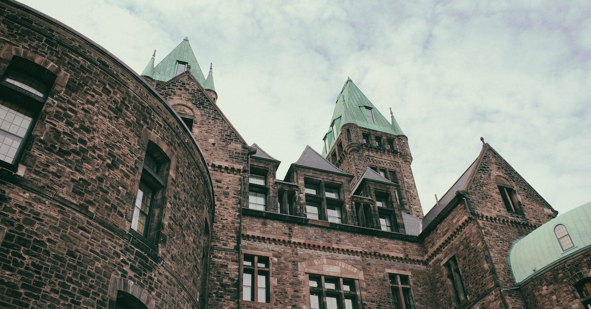 Upward shot of a castle-like building with a green roof on a cloudy day.