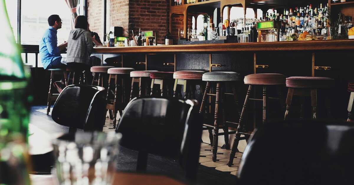 Two people sit on the far end of an otherwise empty trendy restaurant bar