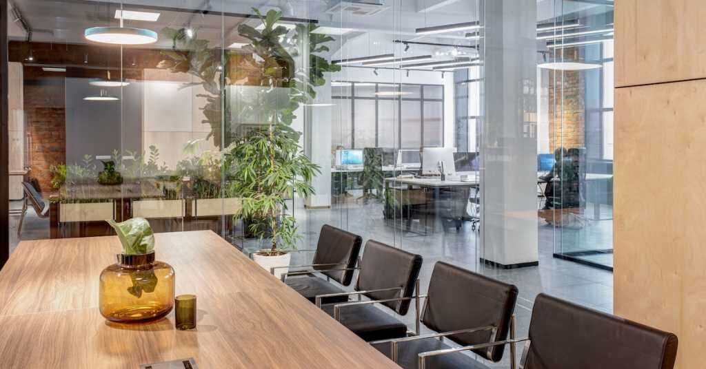 Conference zone in the office in a loft style with brick walls. Zone has a wooden table with black chairs and glass walls