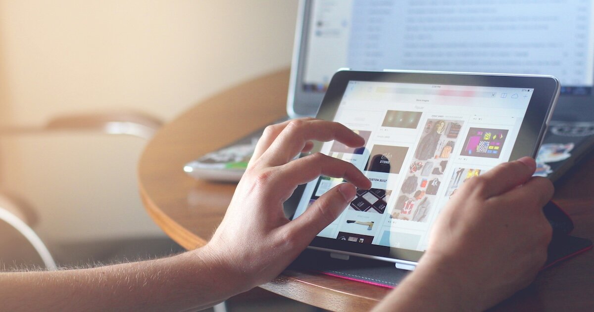 A person is pinching into an image on their ipad, with a computer page open in the background