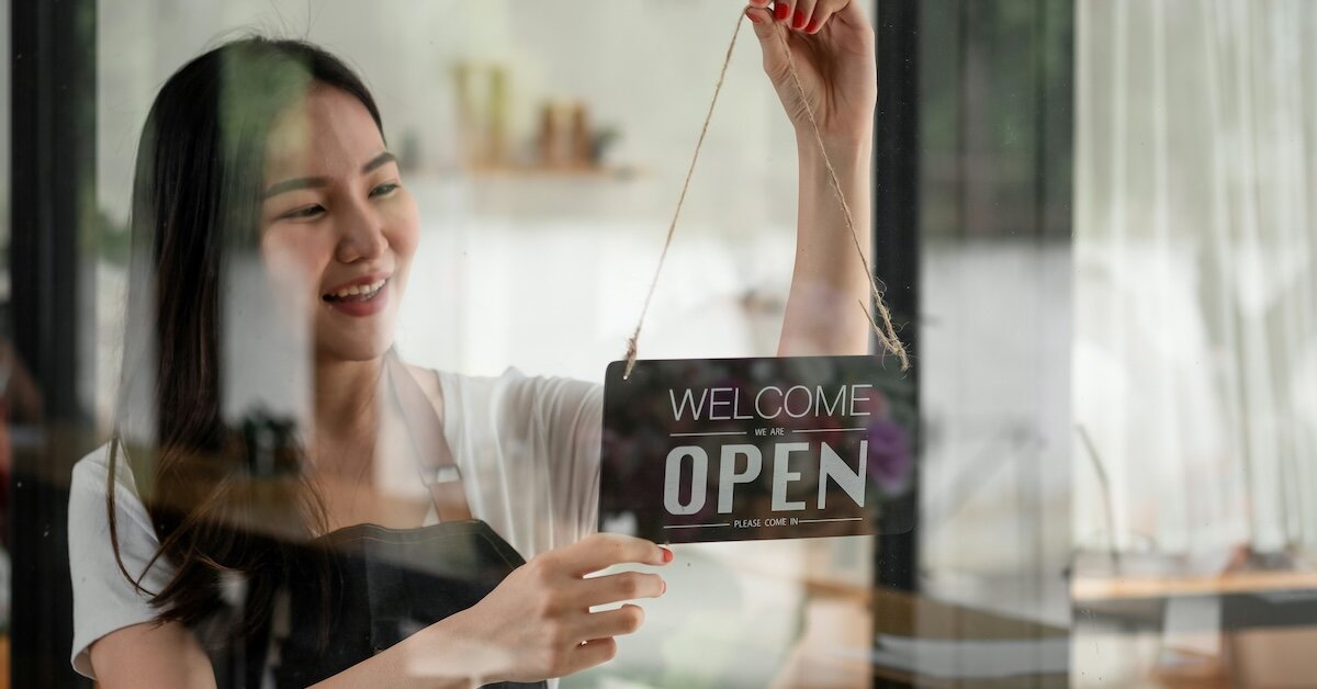 A woman switching a coffee shop sign to open, showcasing the success of a small businesses