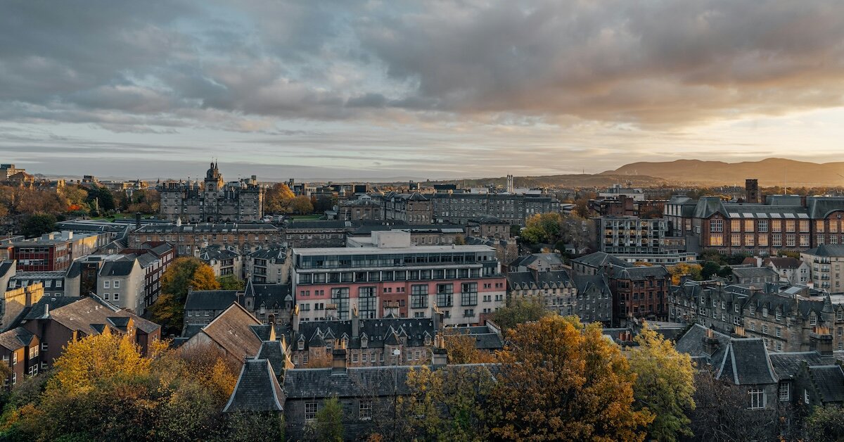 The rooftops of several similar buildings with the coastline and sunset settling over far away mountains