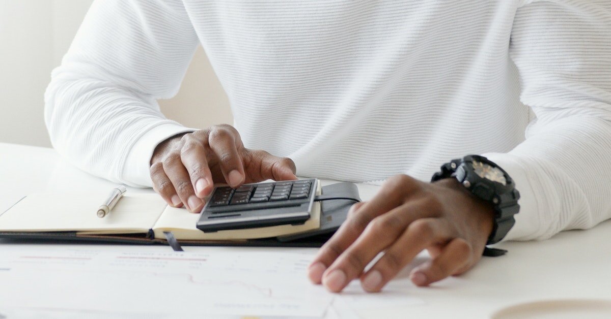 Man in a white shirt tabulates on a calculator while taking notes.