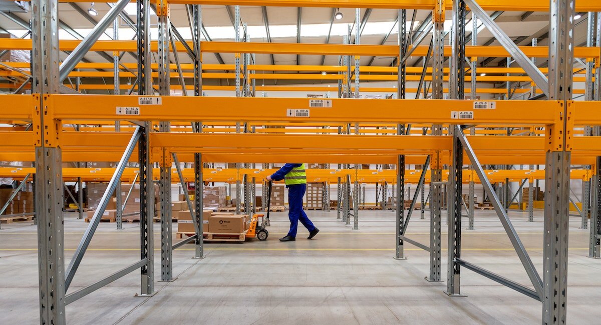 a warehouse worker stands behind shelves, moving a dolly loaded with boxes