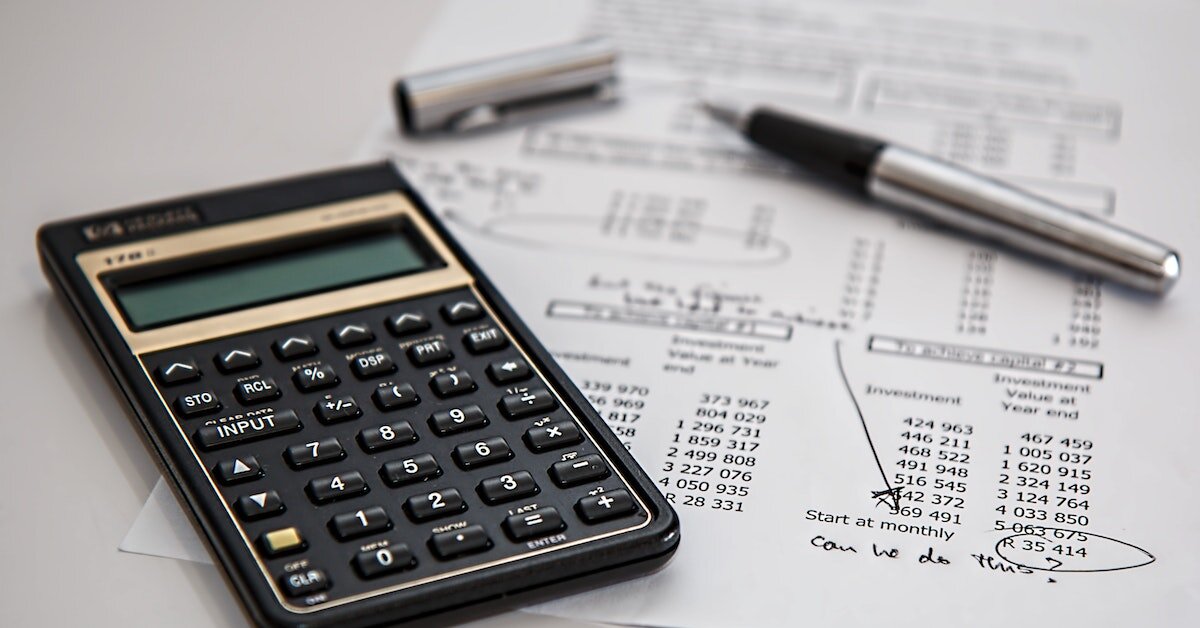 Black calculator on a piece of paper with investment tabulations and a cap and pen.