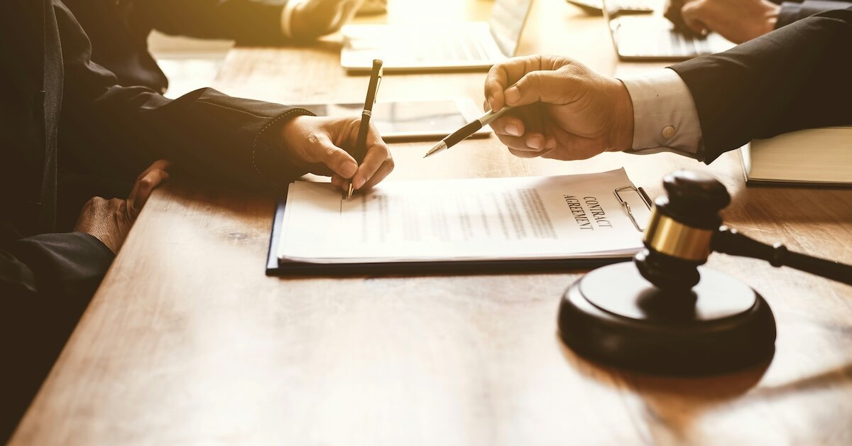 A lawyer points out where another person should sign on a contract agreement