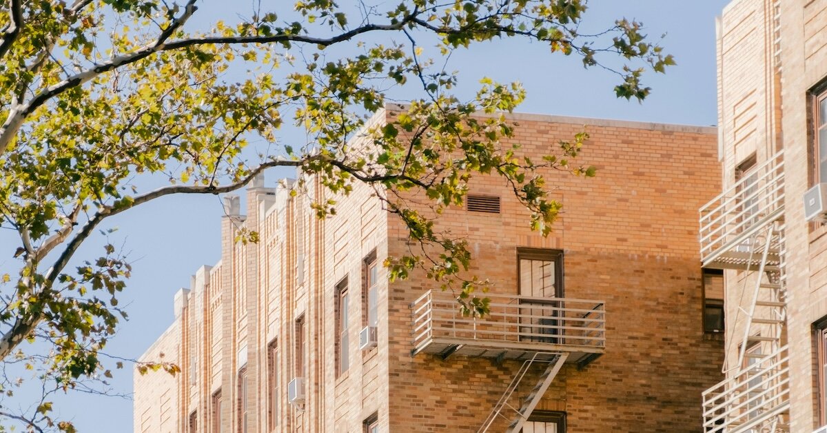 A tree in the foreground frames a brick apartment multifamily building