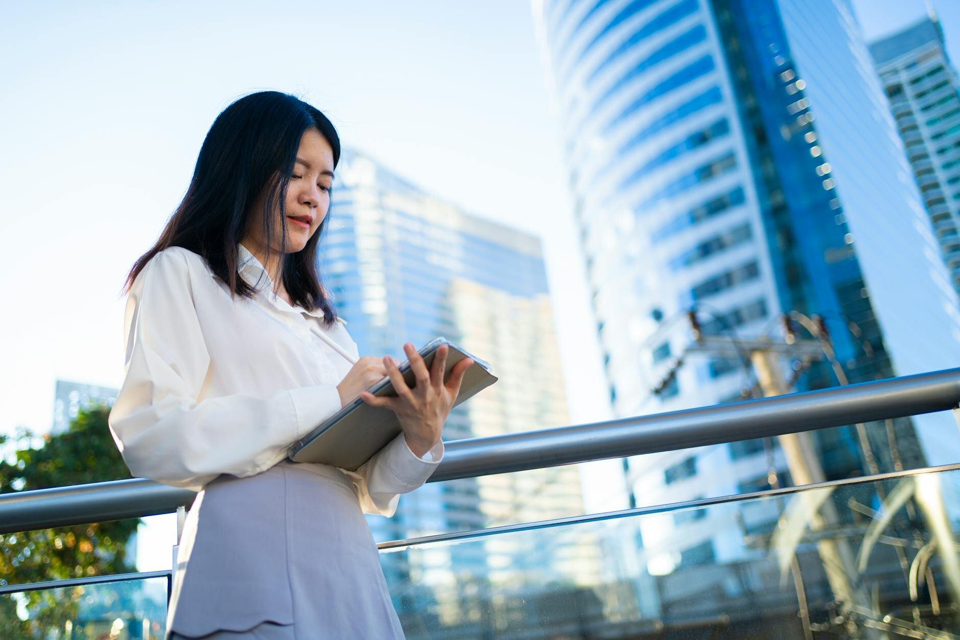 woman looking at a notepad standing in front of tall buildings