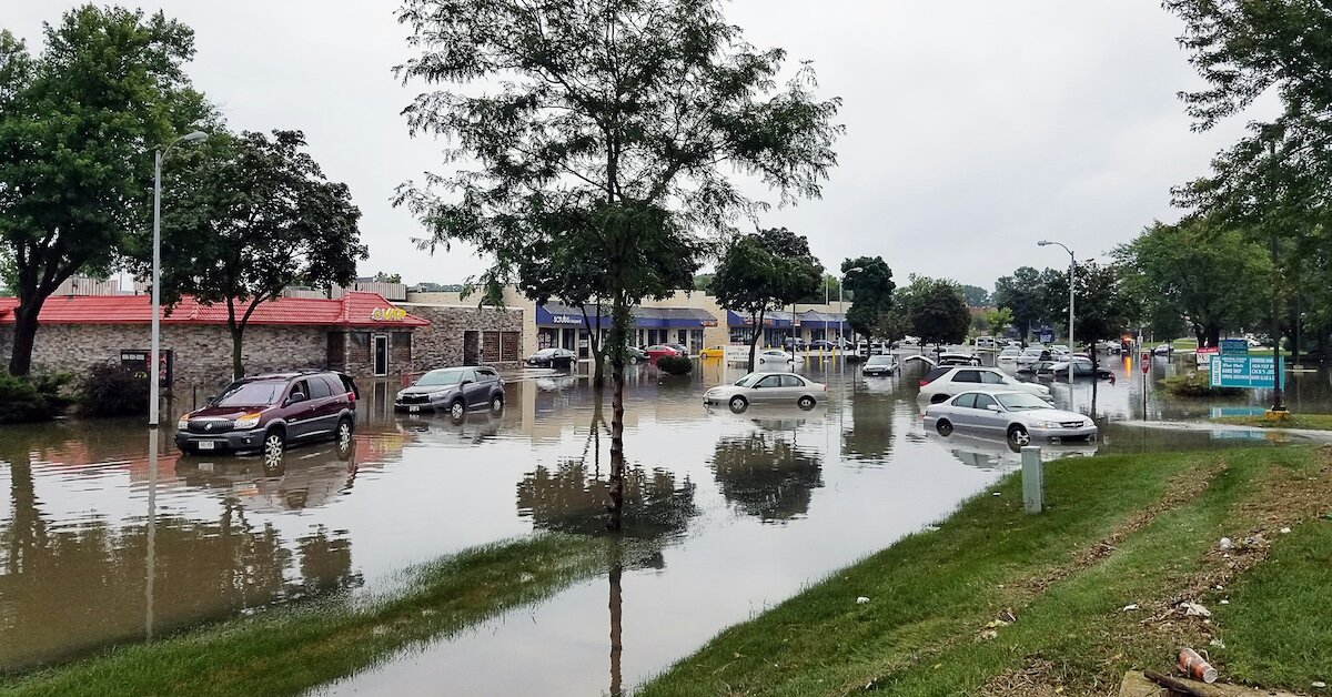 A residential and commercial neighborhood is flooded with water, with cars parked above sporadically