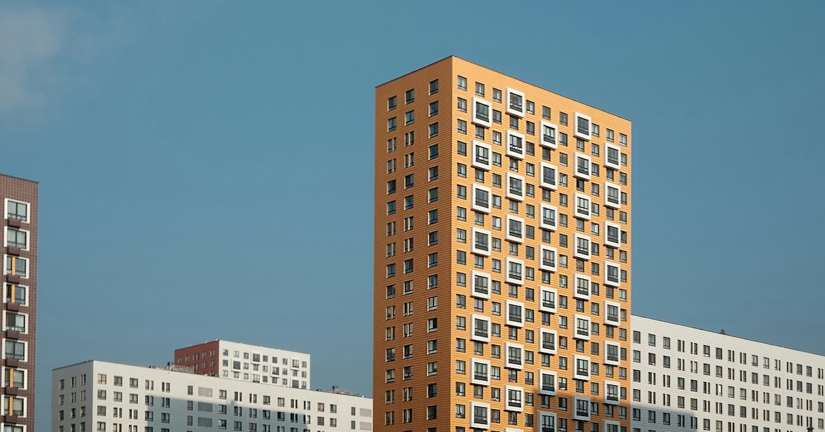 An orange colored building stands against shorter, white concrete buldings