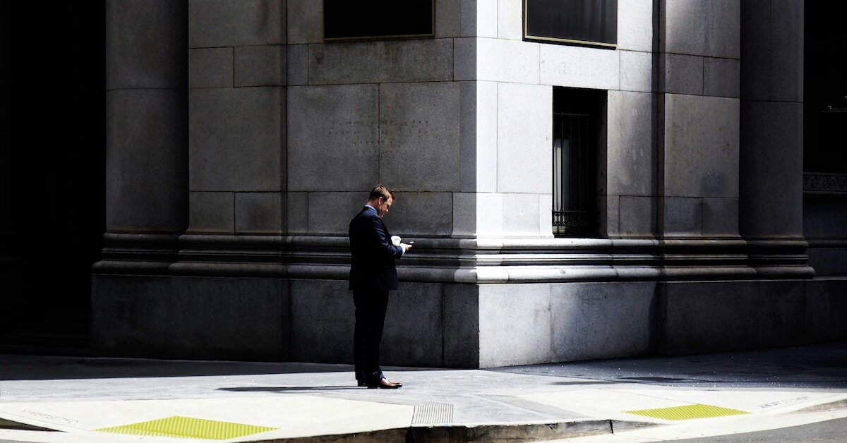 A banker standing outside the building checking something on his phone