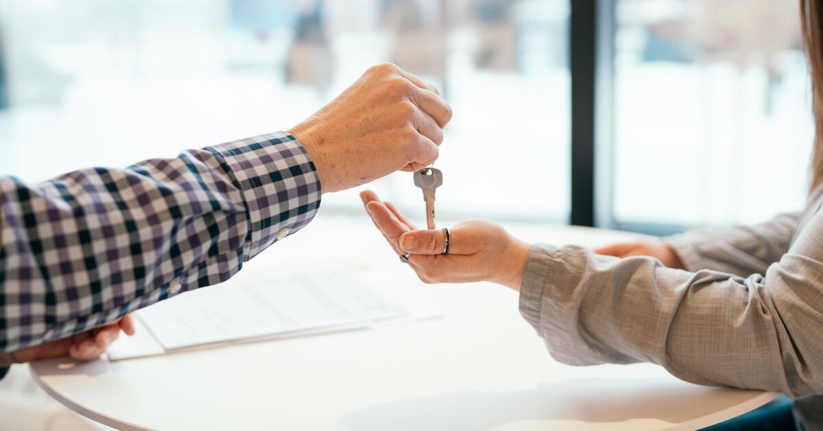 A person hands a pair of keys to someone else across a table with contracts on top of it