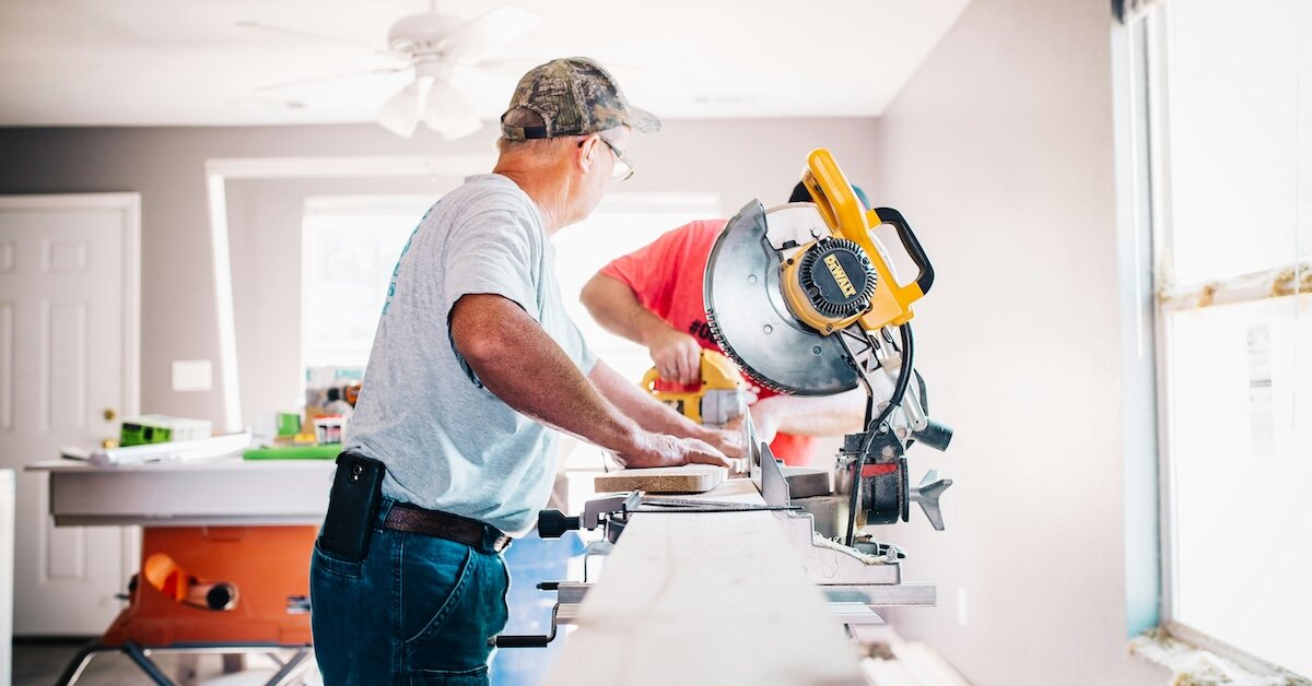 two construction workers operate a saw at a work table