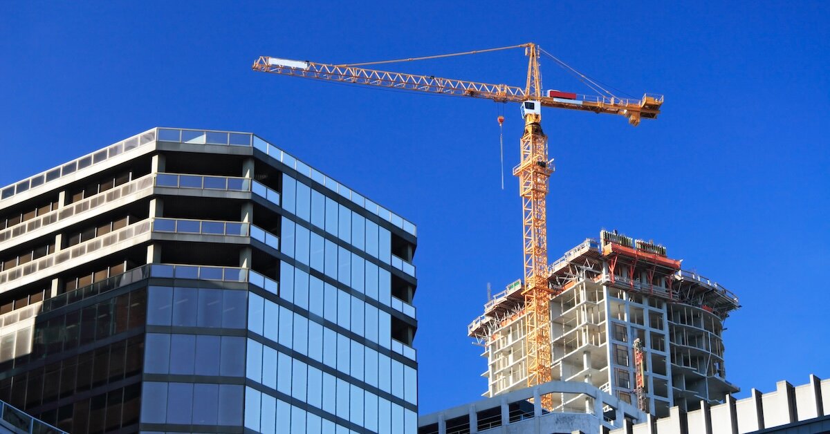 A large construction crane stands above tall commercial buildings