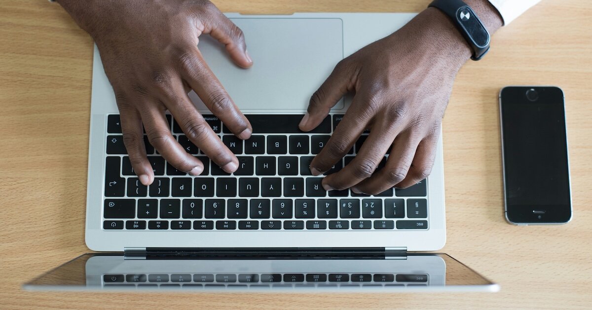 A person typing on their laptop with their iphone off nearby