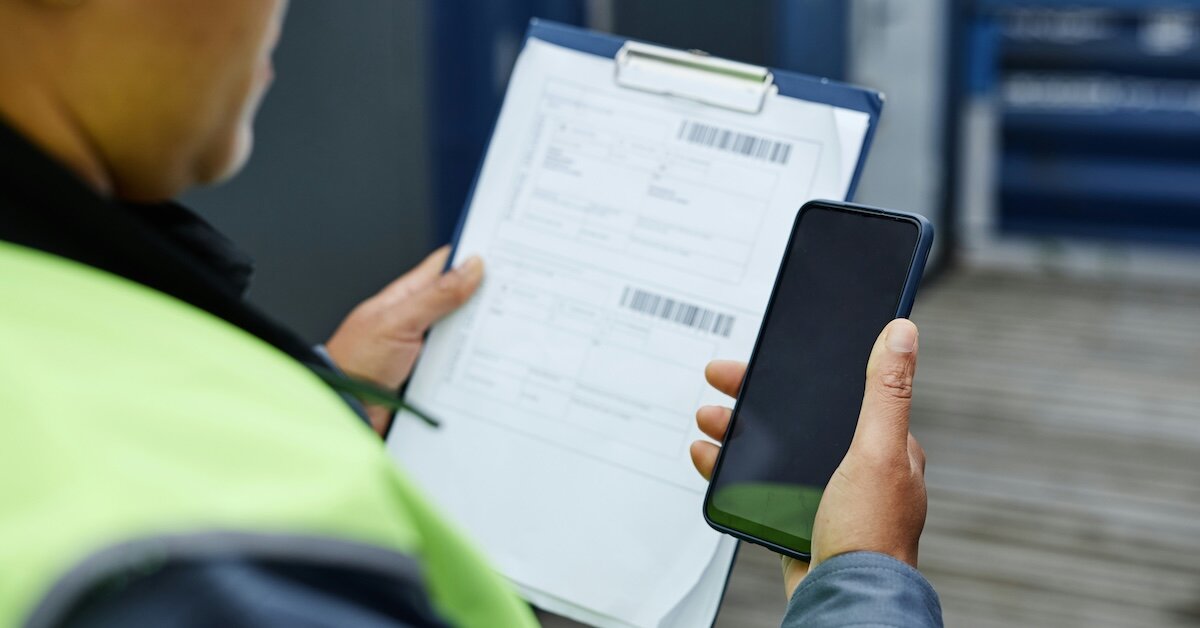 A person checks his phone while holding a checklist on a clipboard