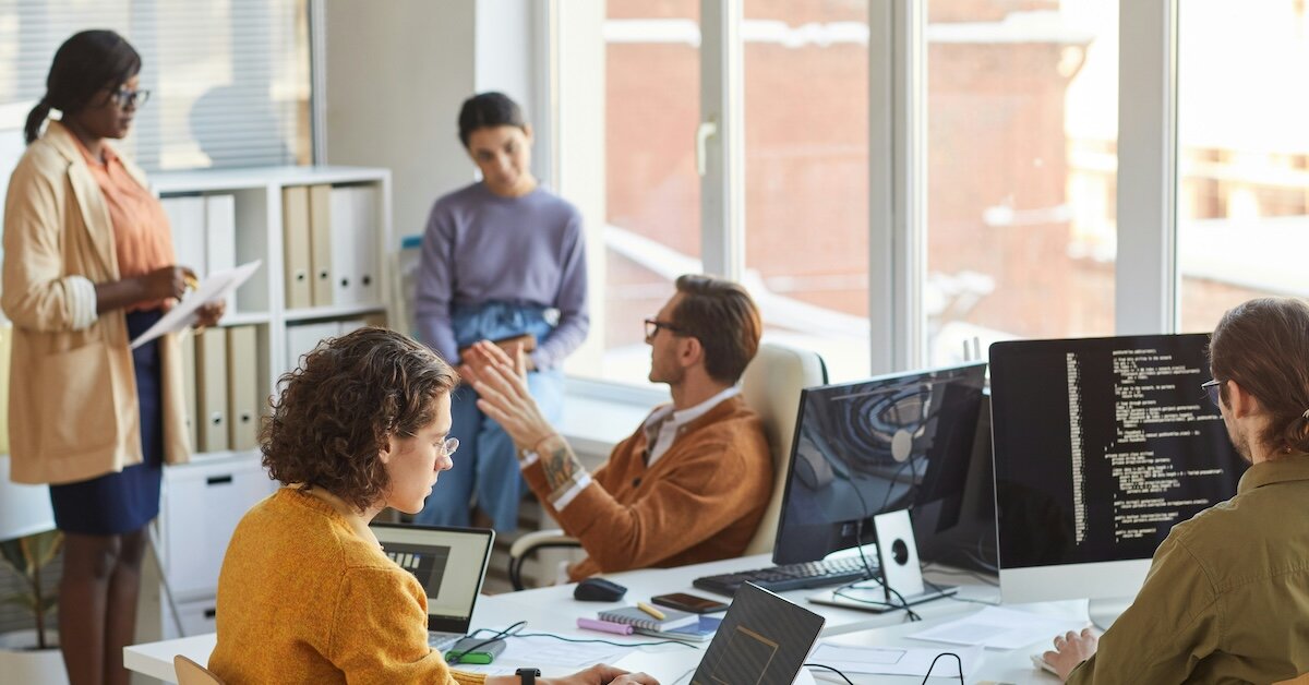 people meeting in the office with a line of code on one person's computer
