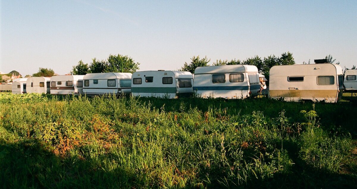 A row of RVs stand in a line with grass in the foreground in an RV Park
