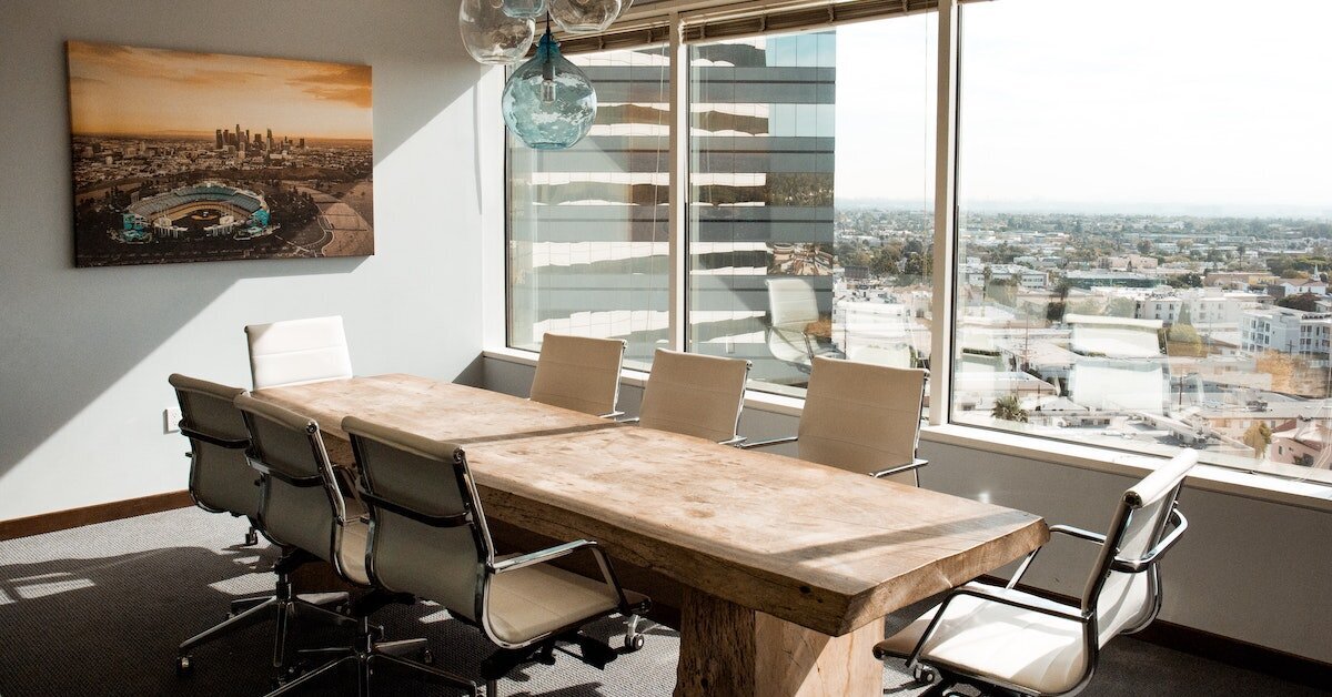 A sun-drenched boardroom centered by a a large wooden conference table.