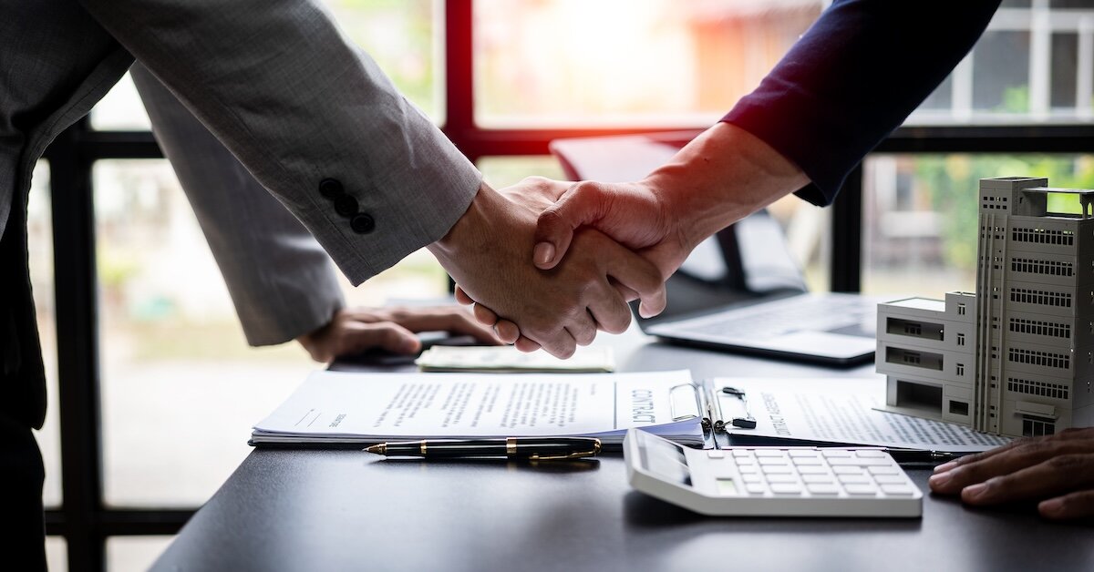 Two professionals shaking hands over a calculator, model building, and business paperwork