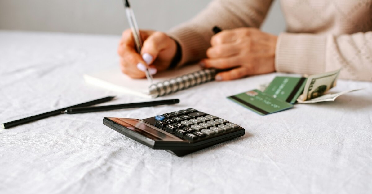 a woman writes down the results from the calculator in the foreground in a notebook