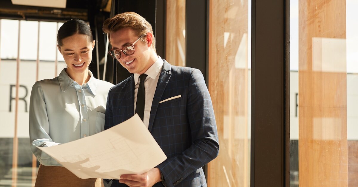 Two professionals review the plans to a commercial office building on a piece of paper