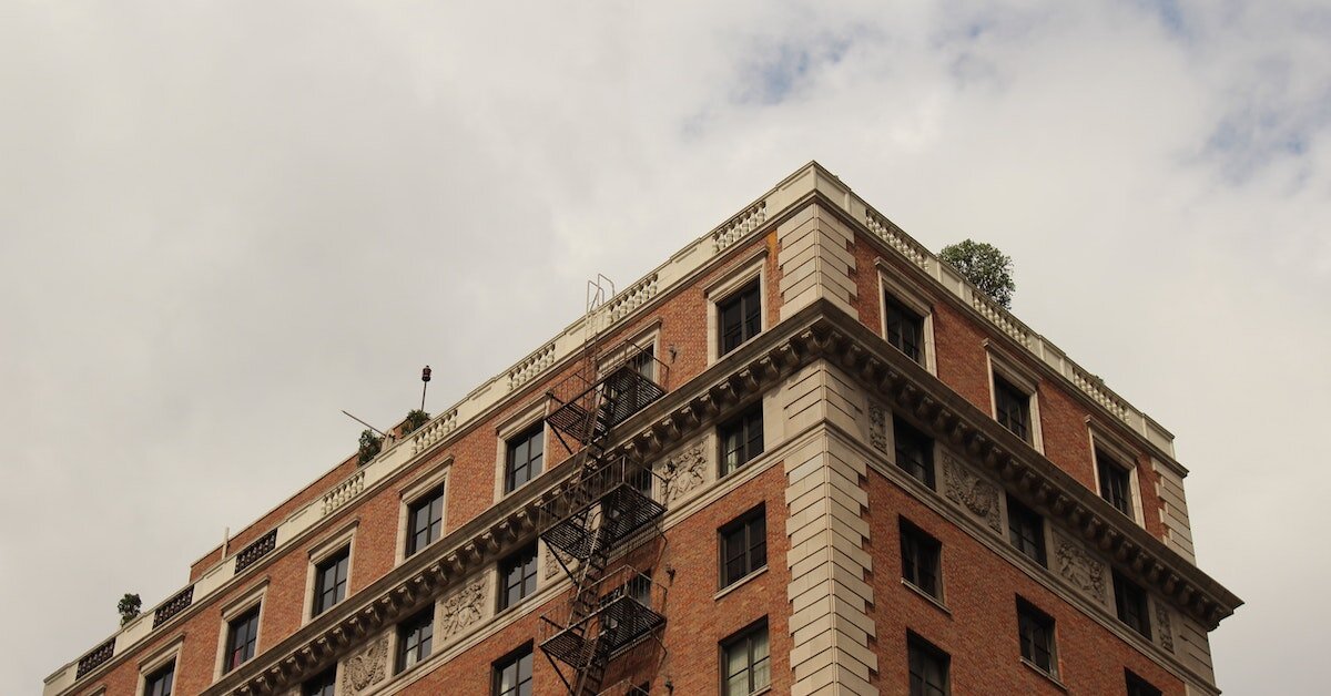 Bottom-up view of a legacy, red-brick apartment building, complete with a fire escape.