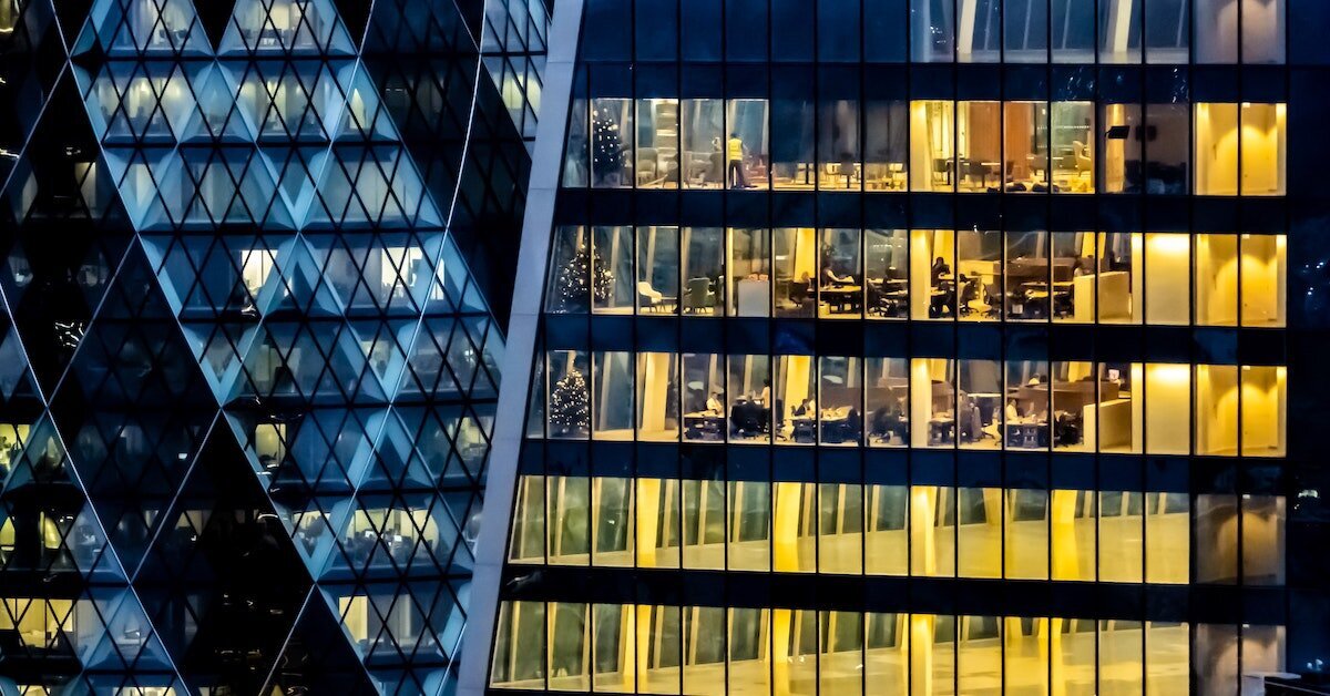 A tall office building at night with lights illuminating the interior through the windows.