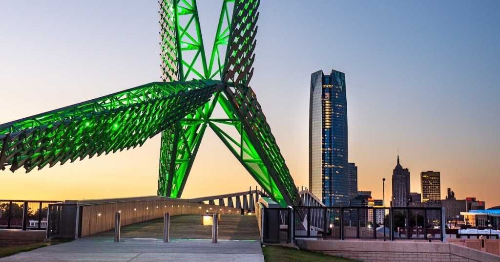 A giant green-list sculpture forms the frame of a bridge across the river from Oklahoma City
