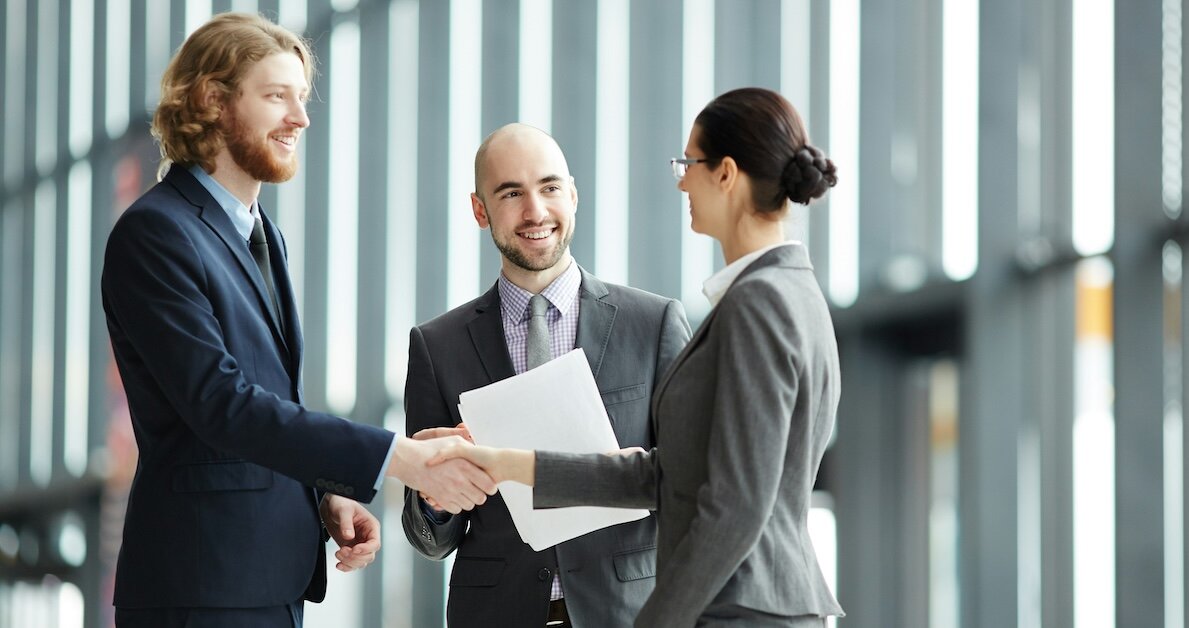 Three professionals introduce each other and shake hands in the lobby of a finance building