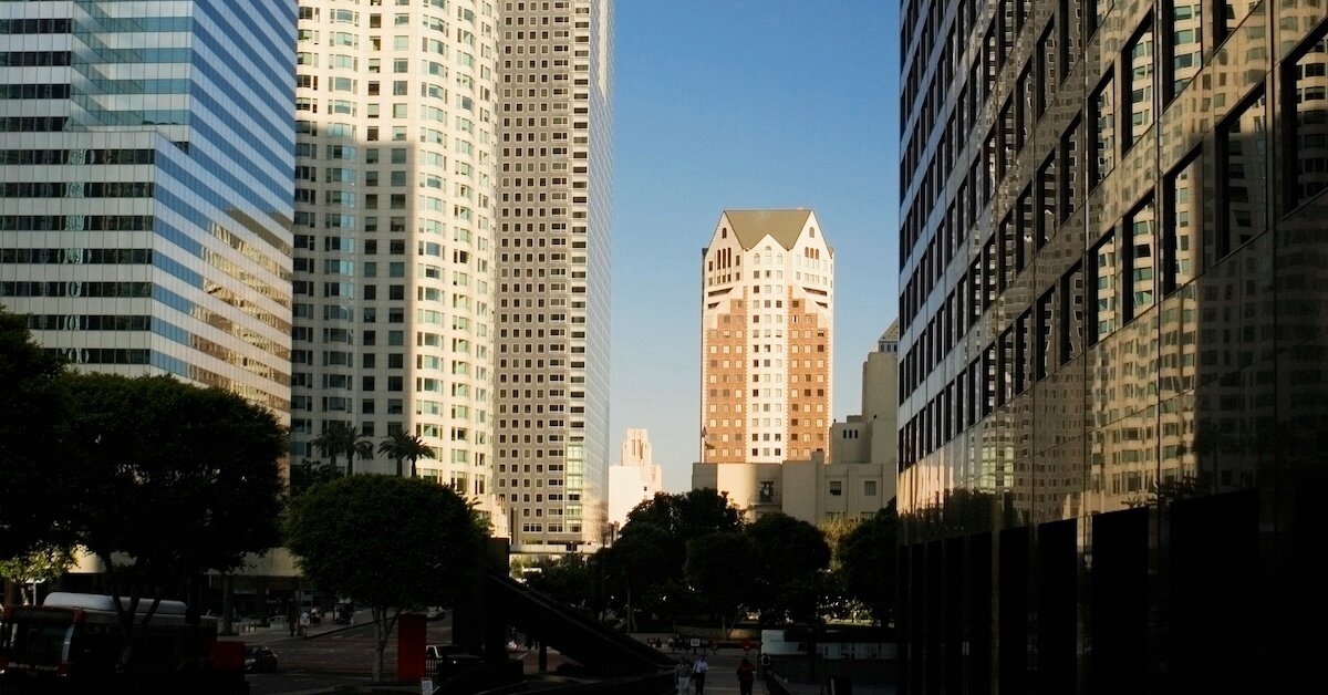A city-level view of a skyscraper framed by tall office buildings in the foreground