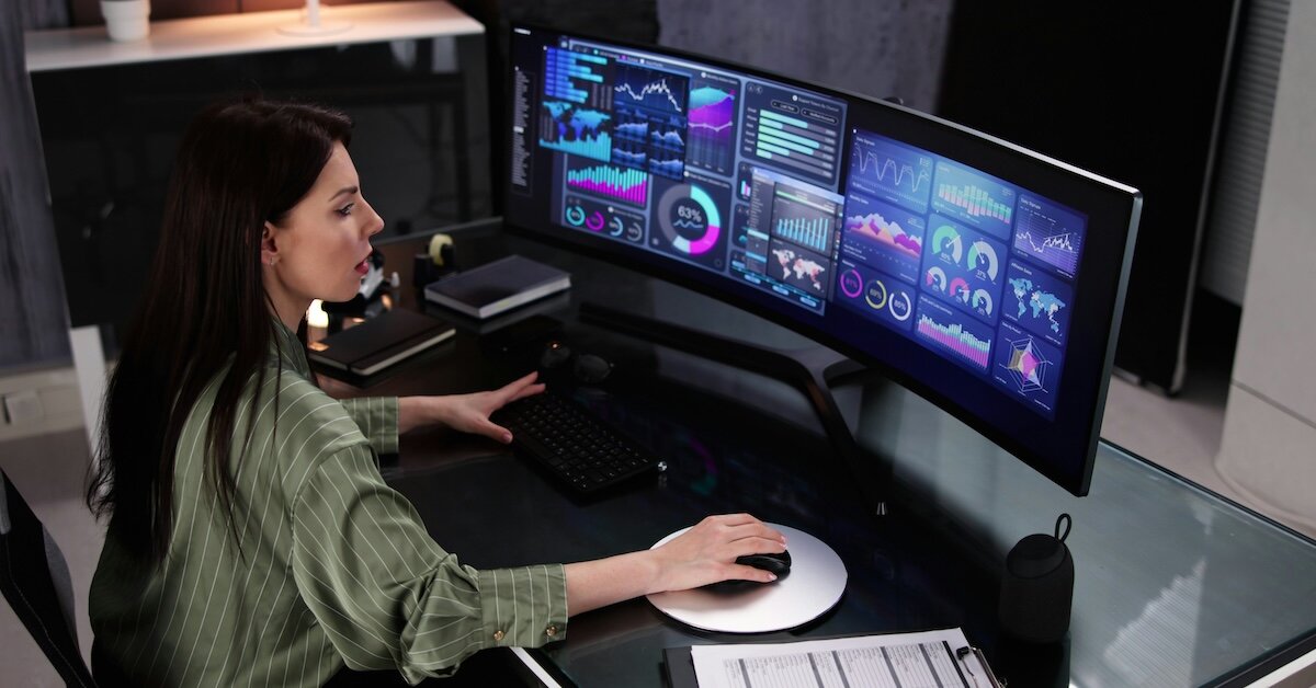 A woman sits in front of a dual screen monitor with various dashboards and data insights