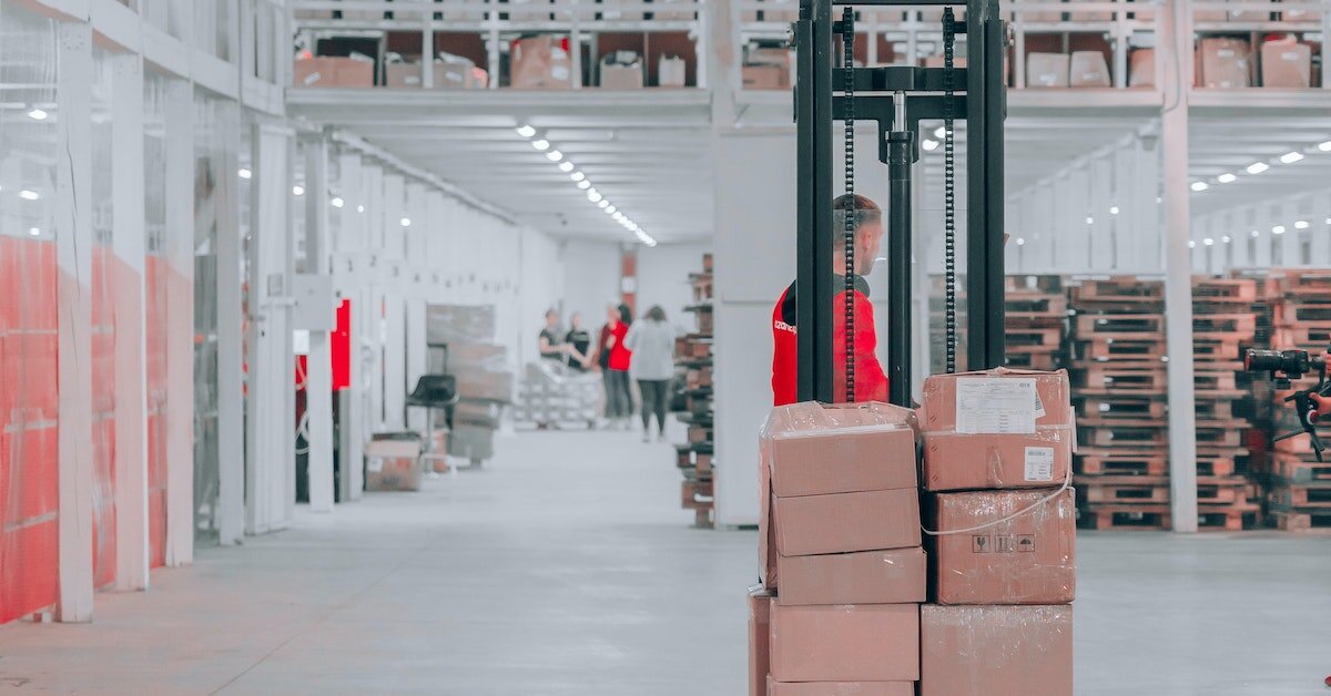 a warehouse employee moves a lift of boxes across the floor