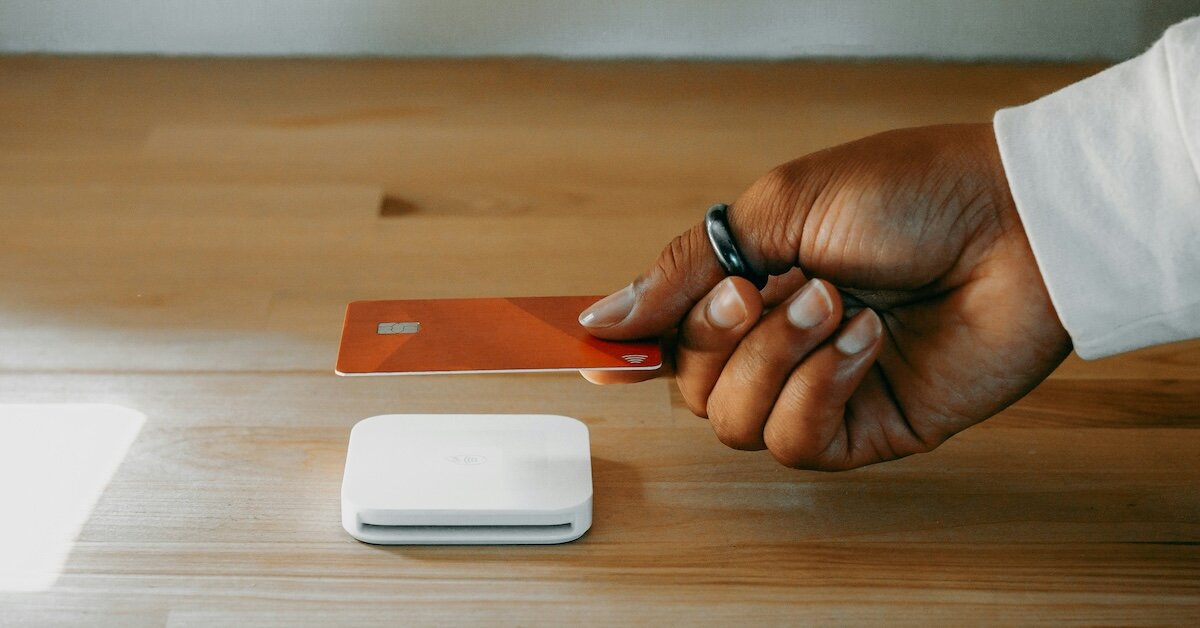 A hand holds a credit card to a square tap-to-pay card reader