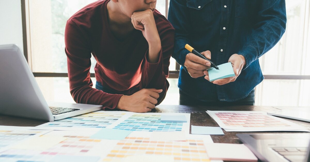 Two people are reviewing color-coded projects with a laptop on the desk