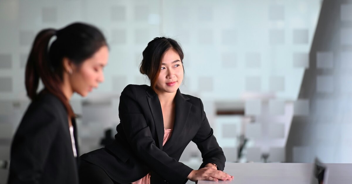 Two professional women sit at a desk for a meeting