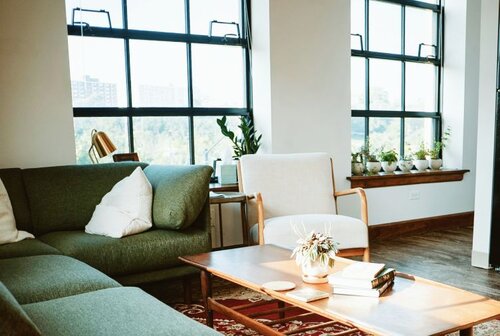 A sunlit room with two windows, a couch, chair, and coffee table