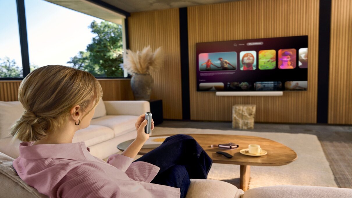 Person sitting on a couch watching a smart TV, holding a remote in a modern living room.