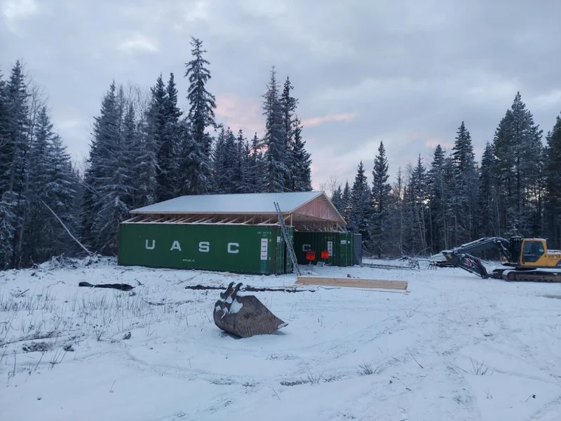 Shipping container building with a timber roof frame in snowy forest