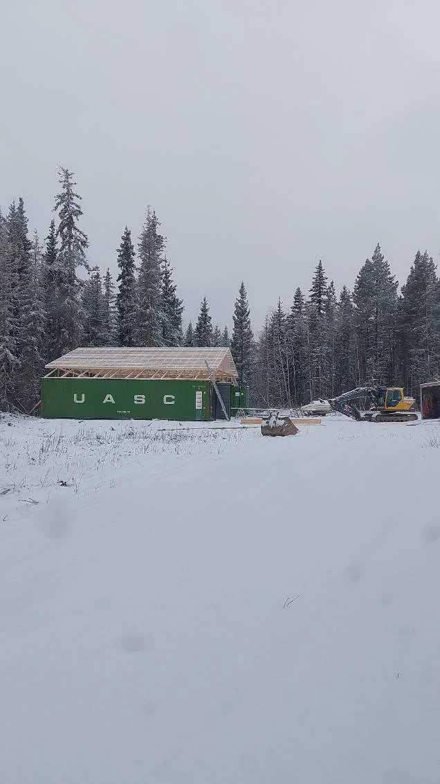 Snowy construction site with a green shipping container and timber roof frame