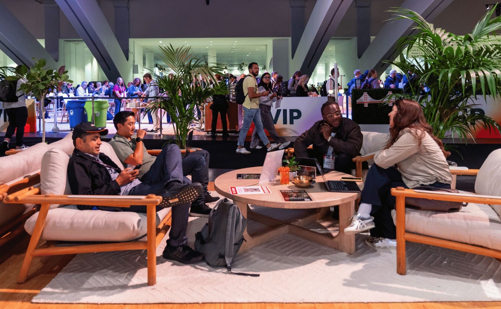 Aerial view of a VIP lounge at a conference or trade show with orange and green seating areas, crowds of attendees below