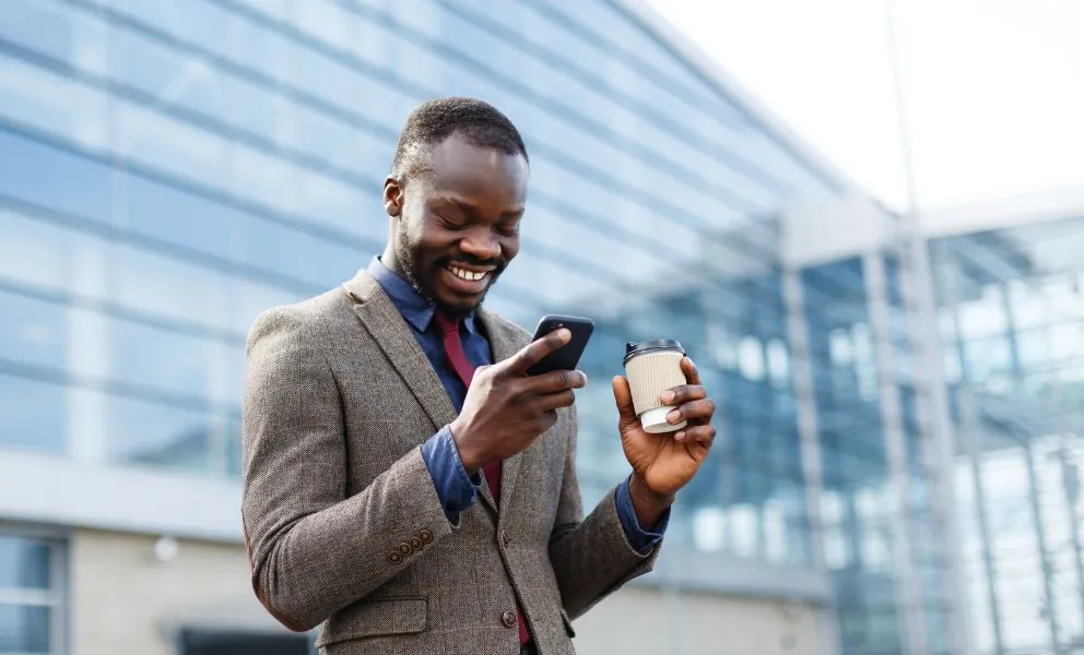 nigerian man in a suit holding coffee and looking at phone