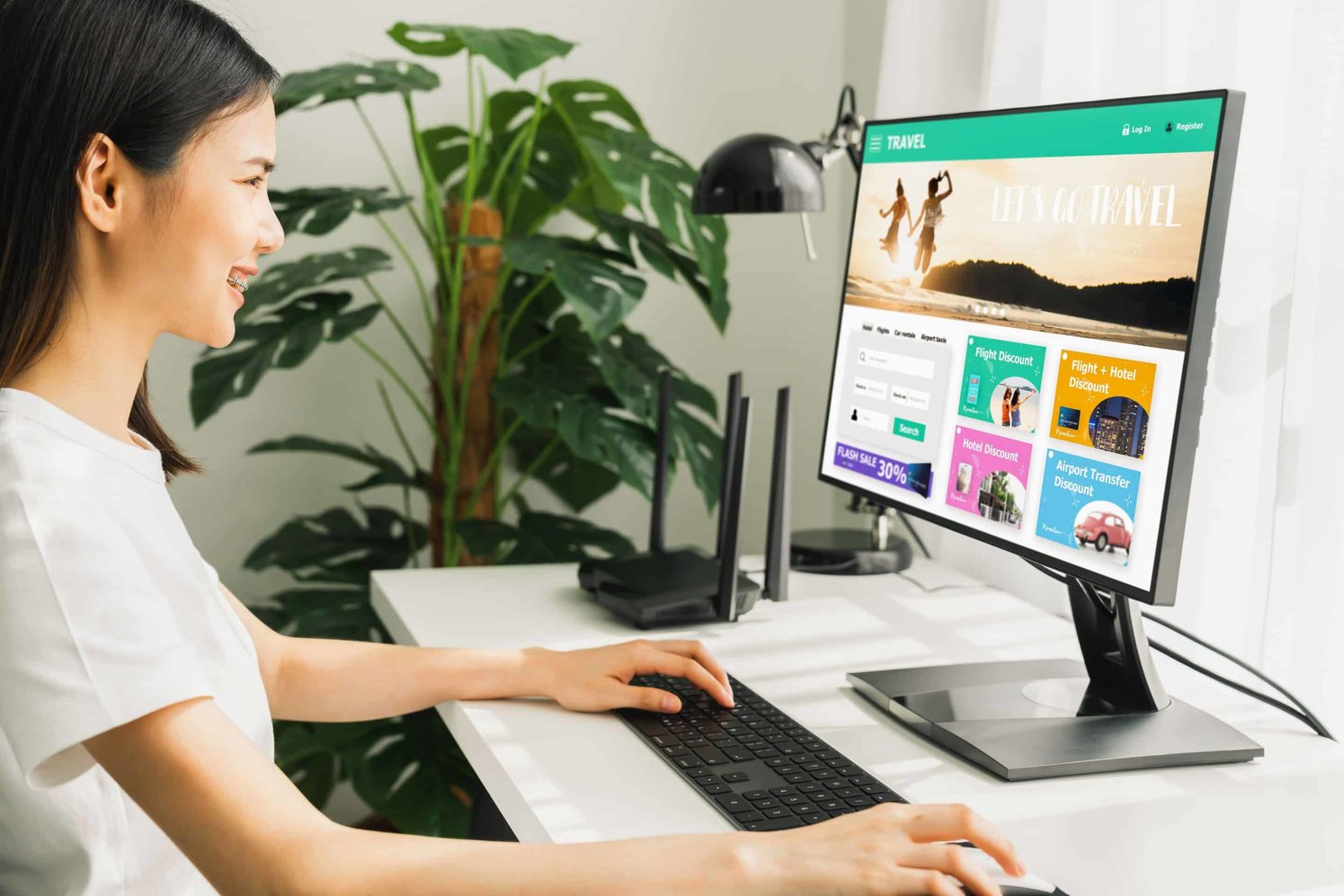 A woman smiling writing on the keyboard of a computer, with the computer screen showing a travel website 