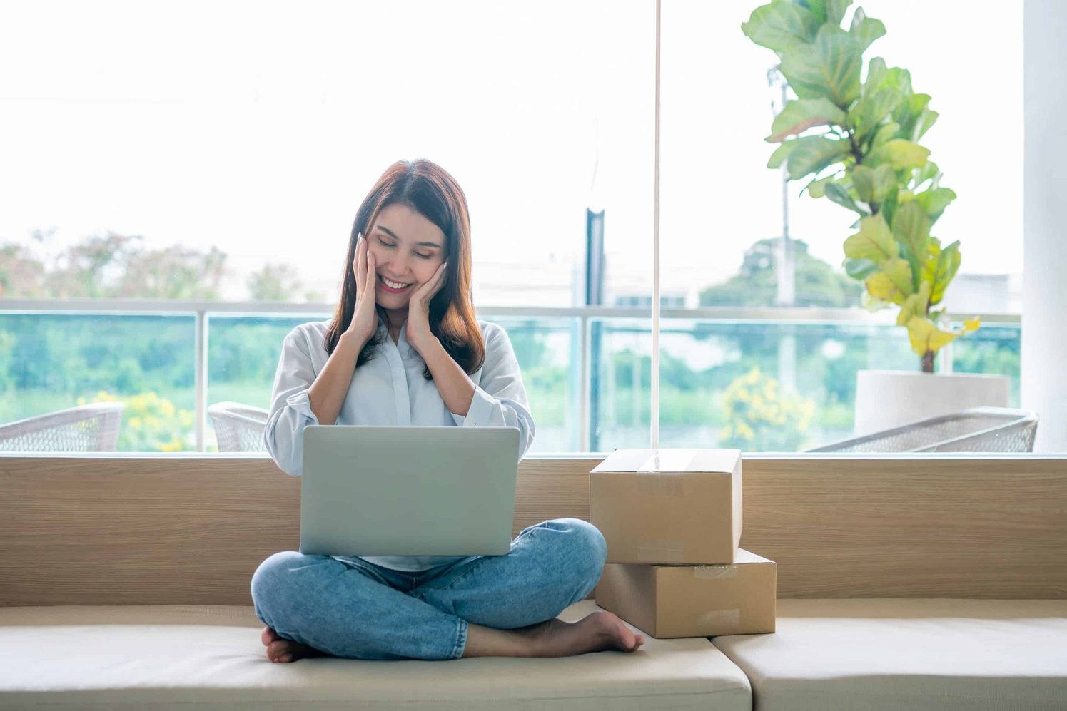 Full body shot of a woman sitting down cross-legged, with a laptop on her knees and smiling 