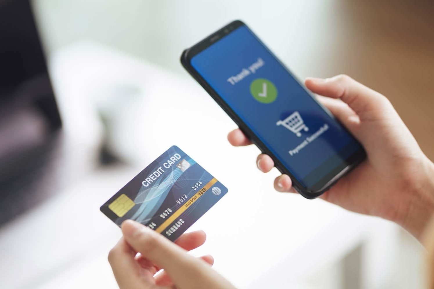 A hand holding a credit card and the other hand holding a phone with a 'Payment Successful' message on the screen.