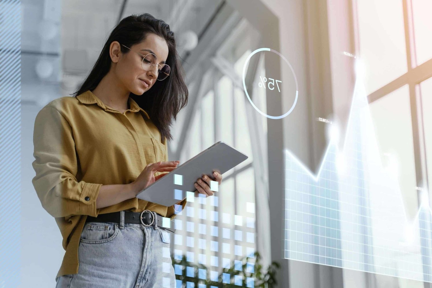 Medium shot of a woman with glasses looking at a tablet. There are holograms graphs around her. 