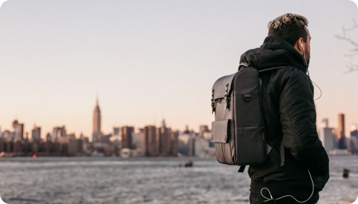 Man carrying a backpack in front of a cityscape near water