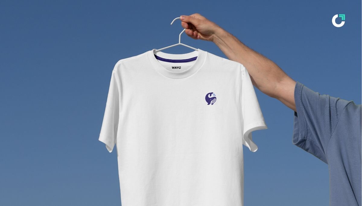 Hand holding a white t-shirt up against the light blue backdrop of the sky