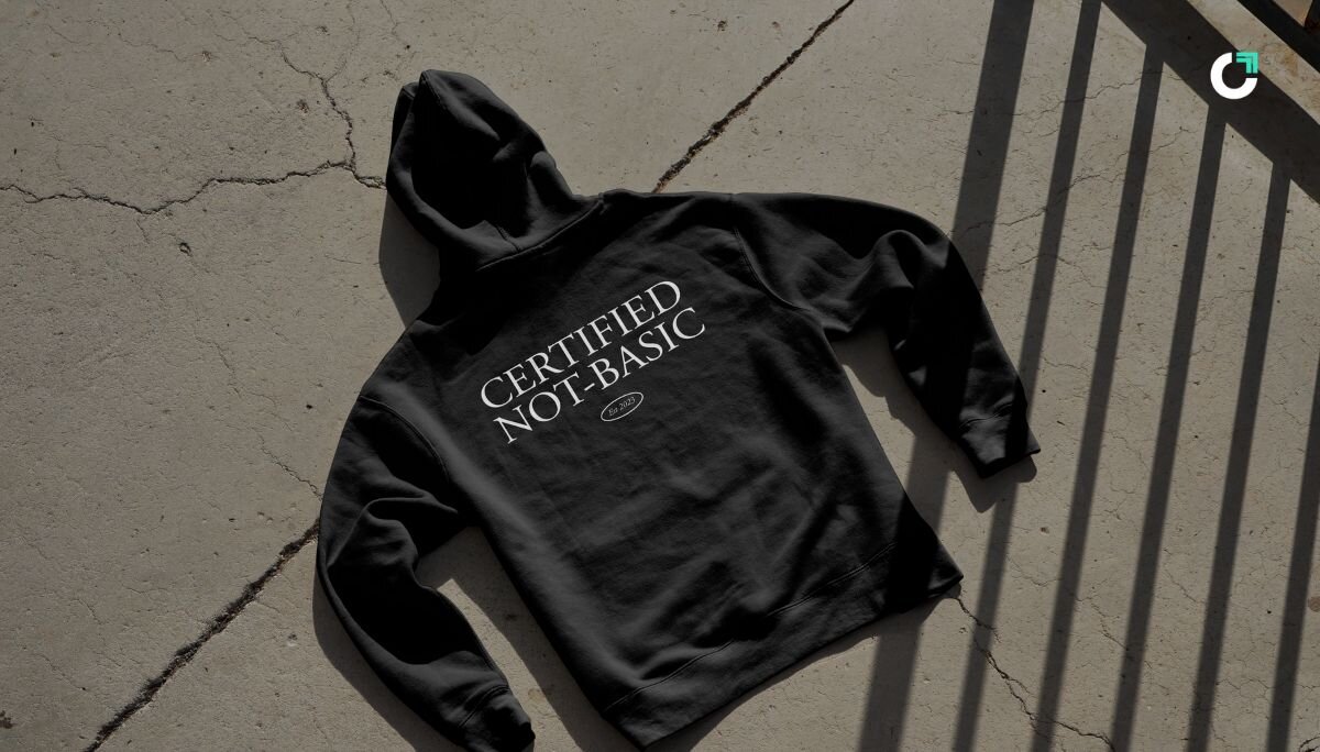 ChatGPT said: Black Wayo hoodie laid flat on sunlit concrete, featuring the bold back print “CERTIFIED NOT-BASIC – Est. 2023” in white serif lettering.